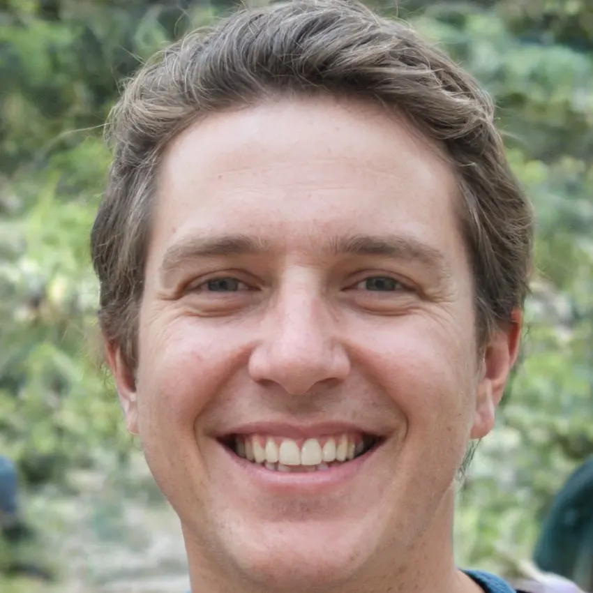 Liam Roberts, a cheerful man with wavy brown hair, smiling widely, surrounded by natural greenery.